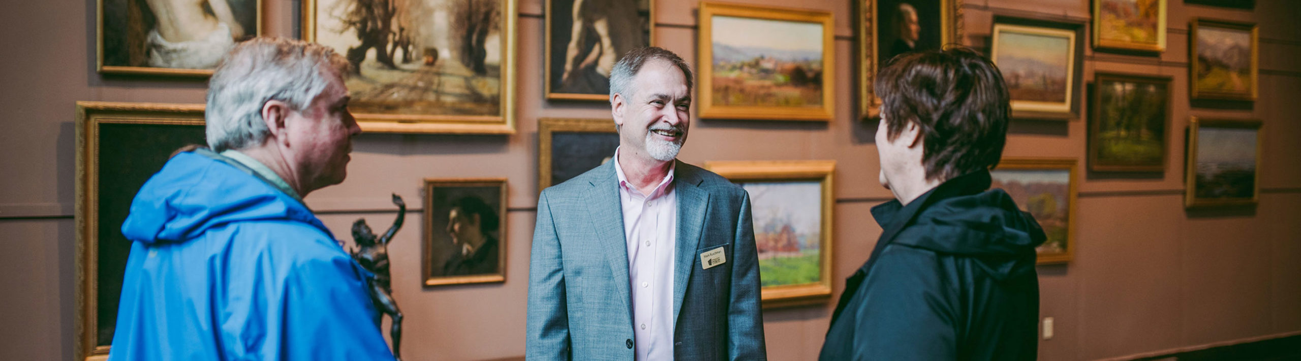Man in jacket standing in front of gallery of paintings