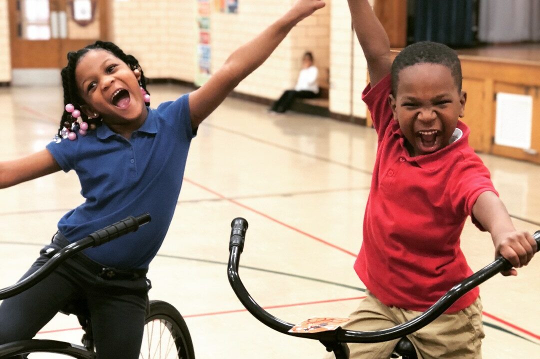 Two children on bikes holding arms up and smiling