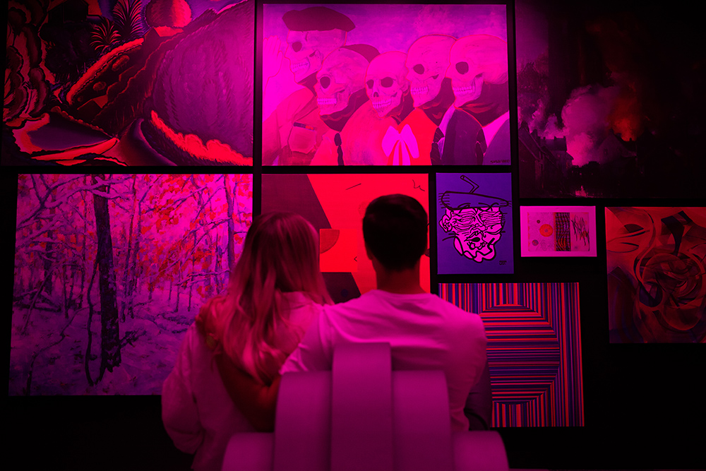 Man and woman sitting in chair together with backs to camera looking at art on walls
