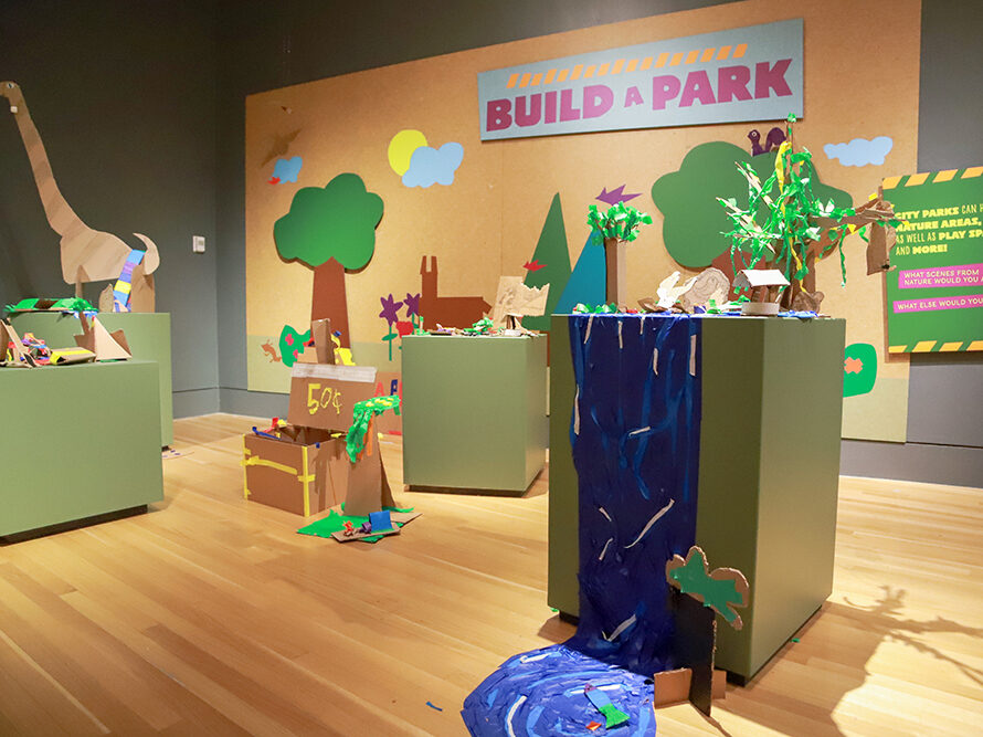 Podiums displaying cardboard creations in front of wall with cardboard designs on it and sign that says build a park