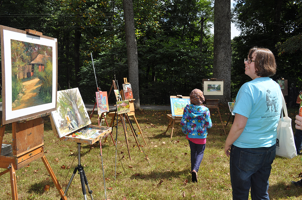 Visitors standing and viewing artwork on easels outside