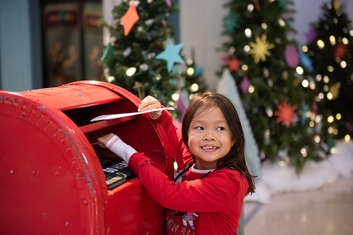 Young girl putting letter to Santa in red mailbox