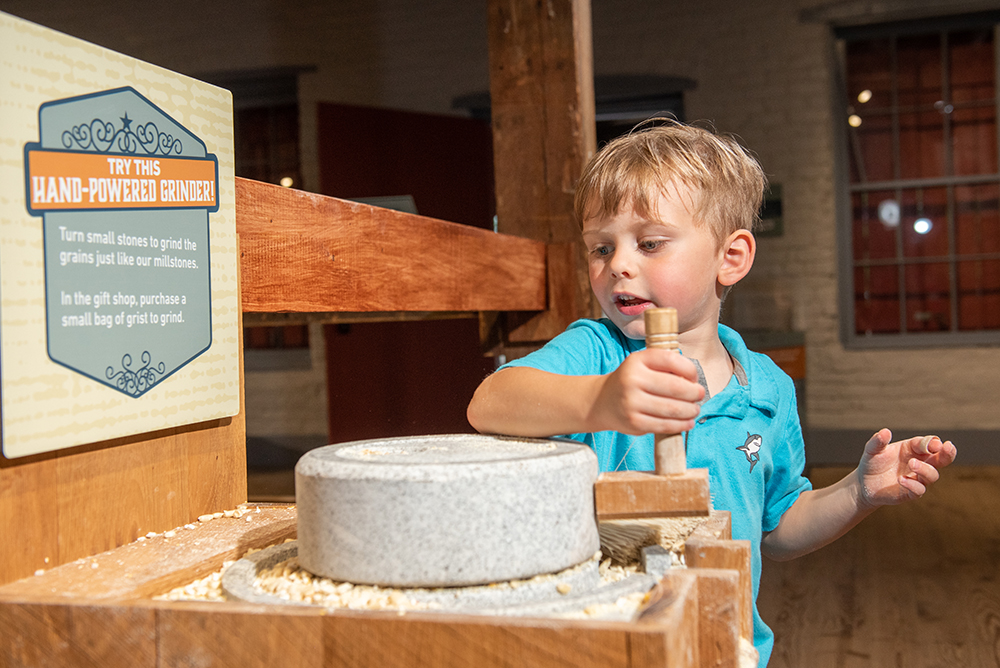 young boy playing with cornmeal grinder