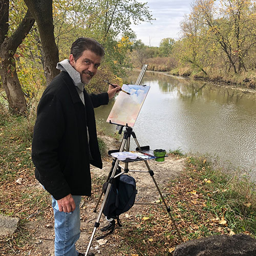 John Kelty standing in front of easel painting river