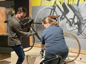 Two people taking bicycle down from being displayed in exhibit