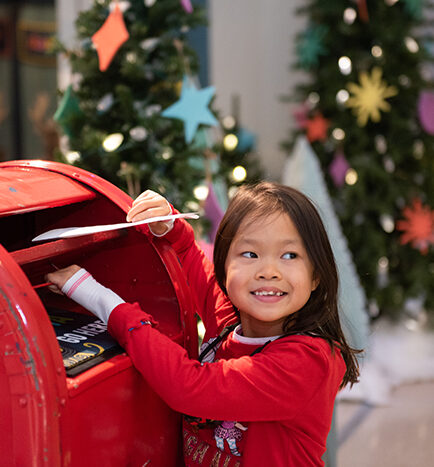 young girl smiling putting letter in mailbox to santa
