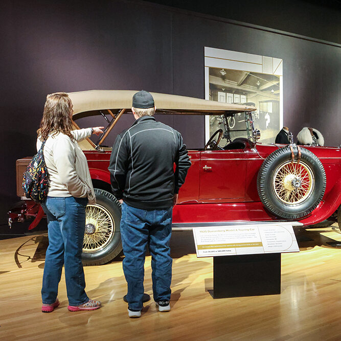 Man and woman looking and pointing at car in exhibit gallery