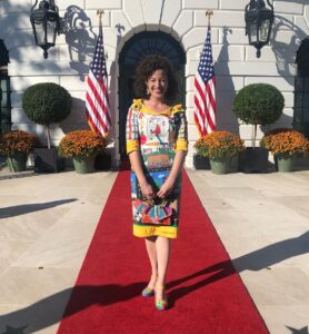 Katie Pourcho poses in front of the White House wearing colorful dress designed by students.