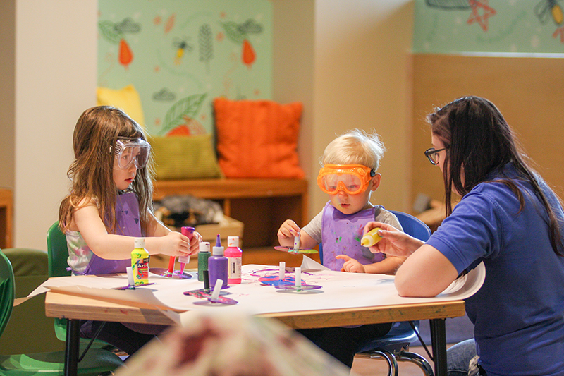 children painting at table with teacher